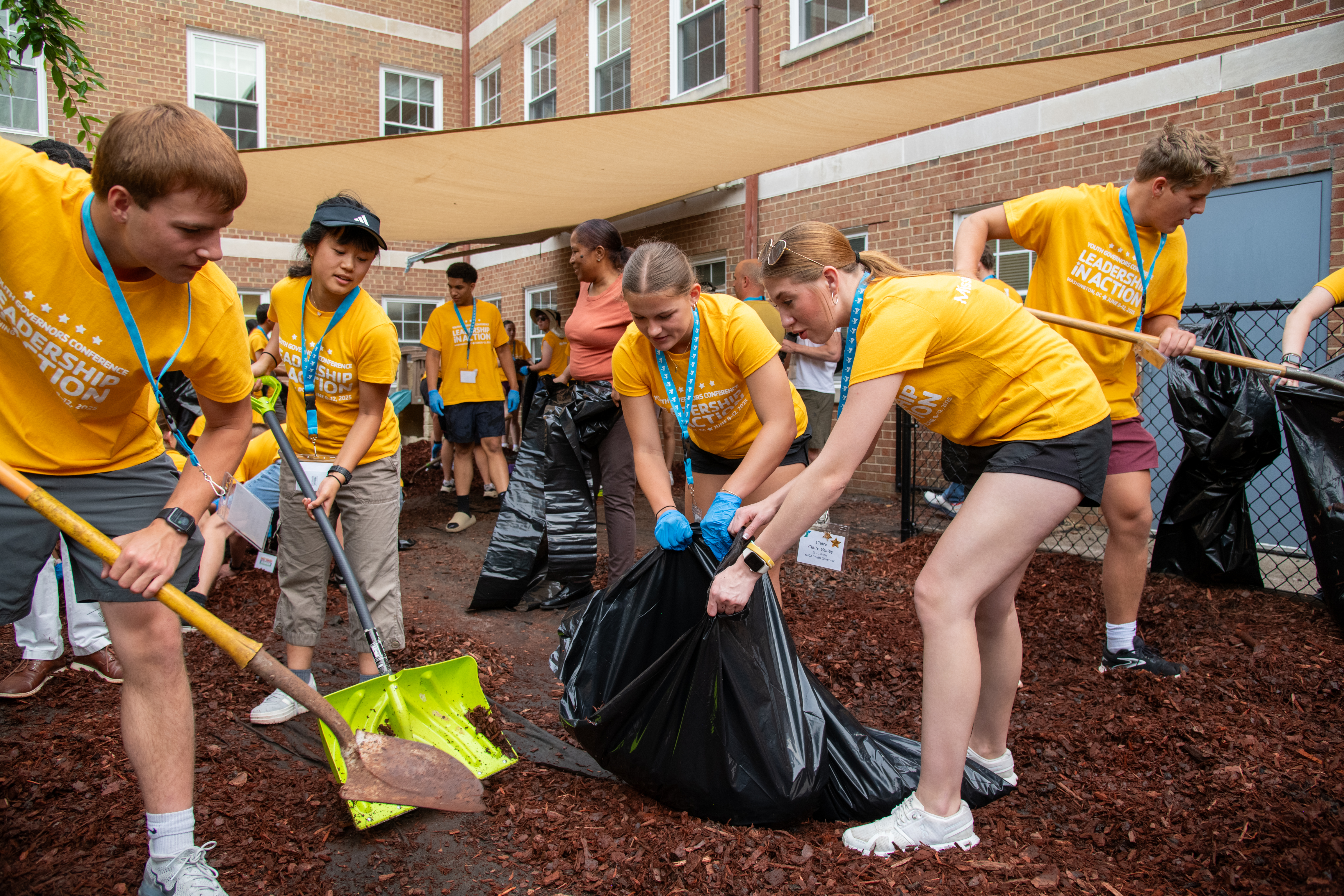 Volunteers in yellow shirts shovel mulch and fill large black bags outdoors